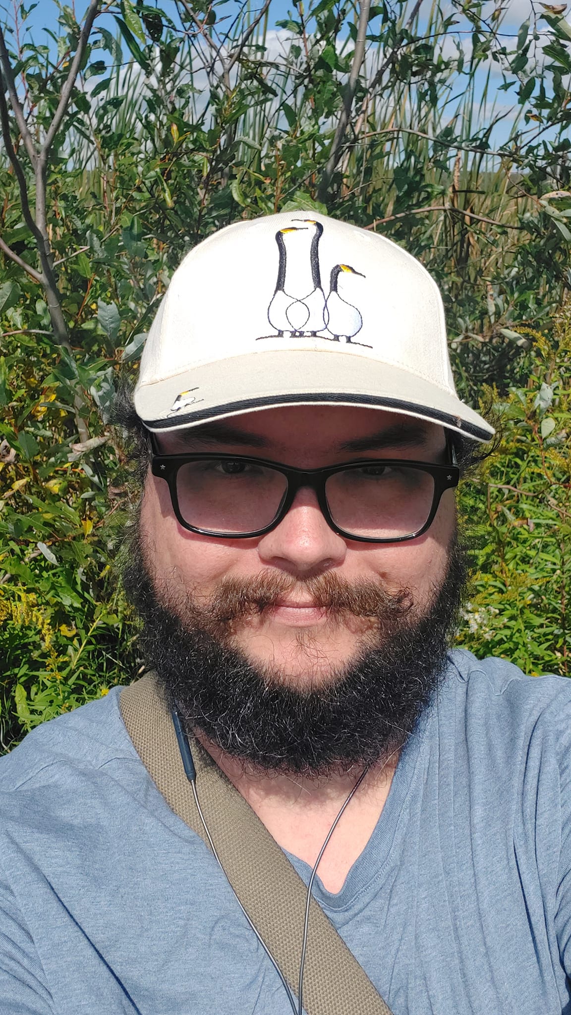 A man with short hair and bushy facial hair stands in front of a some marsh plants